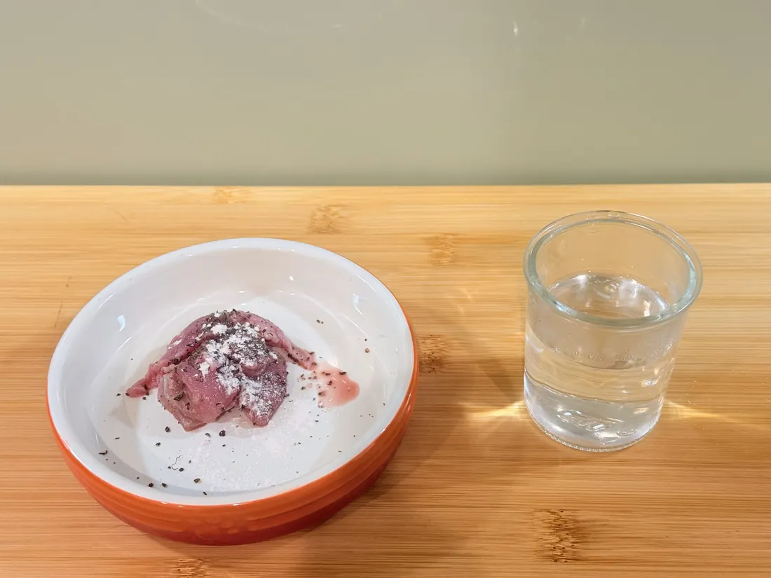 Raw cat food in a bowl beside a glass of water